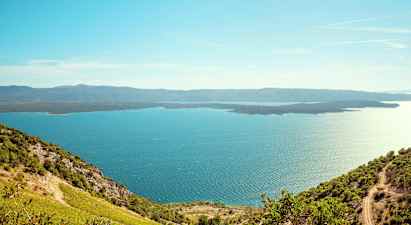 Utsikt över ett blått hav med grönskande kullar i förgrunden och berg i fjärran. (AI-genererad text)