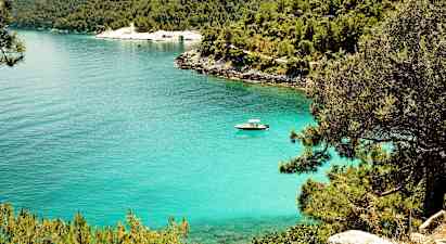 En klarblå vik omgiven av grönska och träd med en motorbåt på vattnet. (AI-genererad text)