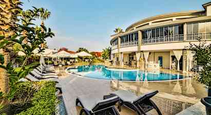 En utomhuspool omgiven av solstolar, parasoller och en modern byggnad. (AI-genererad text)