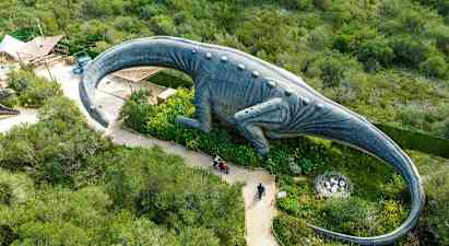 En stor dinosauriestaty omgiven av grönska sedd ovanifrån. (AI-genererad text)