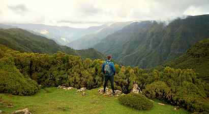 En person står på en grön höjd med utsikt över skogsklädda berg. (AI-genererad text)