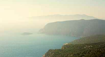 En kustlinje med branta klippor och gröna skogar som sluttar ner mot havet. Ett dis täcker landskapet. (AI-genererad text)