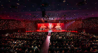 En konsertsal med en upplyst scen där olika musiker framträder inför en publik. (AI-genererad text)