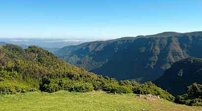 Bilden visar ett landskap med grönskande kullar och berg under en klar blå himmel. (AI-genererad text)