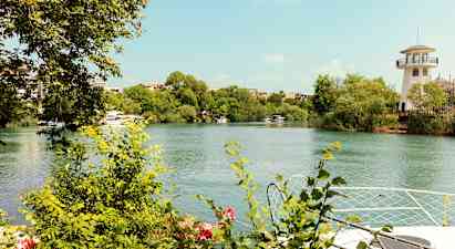 En flod med gröna buskar och träd vid dess kanter. En kejllik byggnad syns på höger sida. (AI-genererad text)