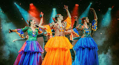 Tre personer klädda i färgglada traditionella dräkter dansar på en upplyst scen. (AI-genererad text)