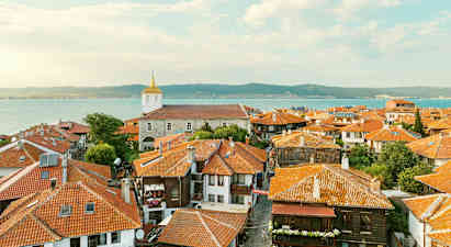 Gamla stadens tak med hus med röda tegeltak och en kyrka i bakgrunden nära havet vid kusten. (AI-genererad text)