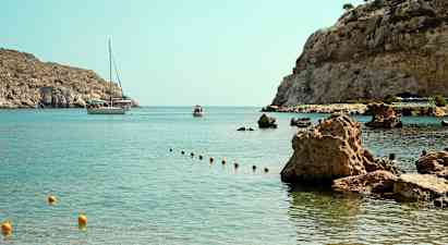 En vik med klara vattnet och steniga kust, där en båt och en mindre flytande farkoster syns i bakgrunden. (AI-genererad text)