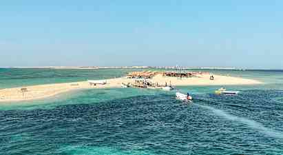 En liten sandö med båtar vid bryggan, omgiven av klart blått vatten. (AI-genererad text)