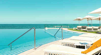 En infinitypool med utsikt över havet, omgiven av solstolar och parasoller. (AI-genererad text)