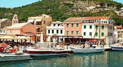 En hamn med flera båtar framför färgglada byggnader och omgiven av kullar. (AI-genererad text)