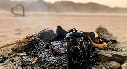 En kaffekanna står vid en slocknad lägereld i en ökenlandskap. (AI-genererad text)