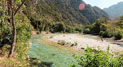 En flod med klart vatten som flyter genom ett grönskande landskap med berg i bakgrunden. (AI-genererad text)