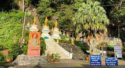 Bild av en trappa som leder upp till flera gyllene buddhistiska statyer och strukturer omgivna av grönska. (AI-genererad text)