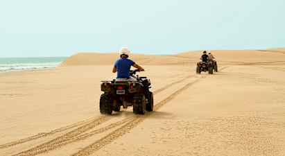 Två personer kör fyrhjulingar över en sandstrand med havet i bakgrunden. (AI-genererad text)