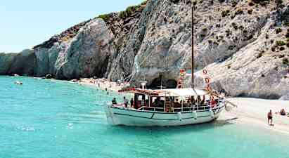 En båt ligger förtöjd vid en strand med klippor och klart turkosblått vatten. (AI-genererad text)