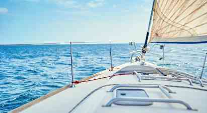 Närbild på fördäcket på en segelbåt, med vit segelduk och blått hav i bakgrunden. (AI-genererad text)