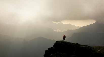 En vandringsman står på en bergstopp med dimmiga dalar och berg i bakgrunden. (AI-genererad text)
