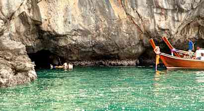 Personer simmar i vattnet vid en klippa, och två träfartyg flyter nära. (AI-genererad text)