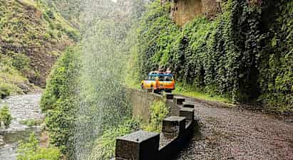 En gul-orange jeep på en väg vid ett vattenfall i en grön dal. (AI-genererad text)