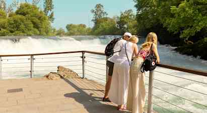 Tre personer lutar sig mot ett räcke och blickar ut över ett vattenfall. (AI-genererad text)