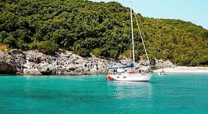 Segelbåt på turkost vatten nära en grönskande strand. (AI-genererad text)