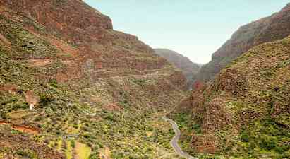 En smal väg slingrar sig fram genom en dal omgiven av branta berg med grön vegetation. (AI-genererad text)