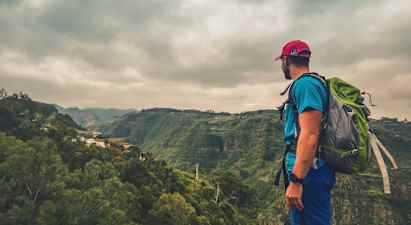 En person med ryggsäck står och tittar ut över en grön dal under molnigt väder. (AI-genererad text)