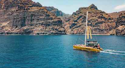 En katamaran seglar nära höga klippor, med klarblått vatten i förgrunden. (AI-genererad text)