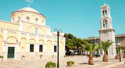 En gul byggnad med kupol och en klocktorn samt palmer och gatlykta. (AI-genererad text)