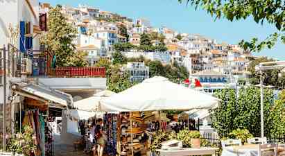 En pittoresk stadsbild med vita hus med röda tak på en sluttning, parasoll och försäljningsstånd i förgrunden. (AI-genererad text)