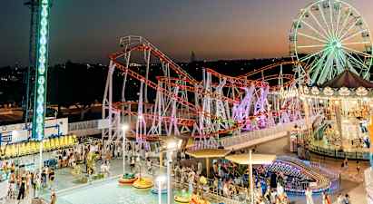 En kvällsbild av en livlig nöjespark med en stor pariserhjul, en färgglad berg- och dalbana och en pool med radiobilar. (AI-genererad text)