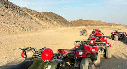 En rad fyrhjulingar står parkerade på en ökenväg, omgivna av sandiga kullar. (AI-genererad text)