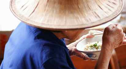 En person i blå klädsel och en hatt äter från en skål med sked. (AI-genererad text)