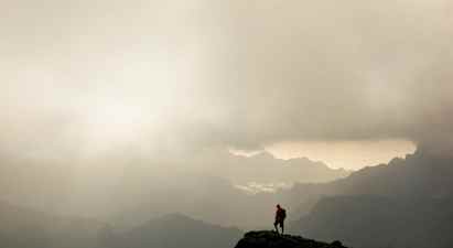 En vandringsman står på en bergstopp med dimmiga dalar och berg i bakgrunden. (AI-genererad text)