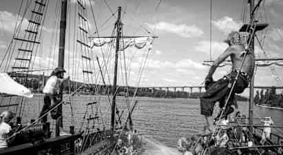 En scen på en gammaldags piratskepp med människor som interagerar och vattenspridning mellan båtar. (AI-genererad text)
