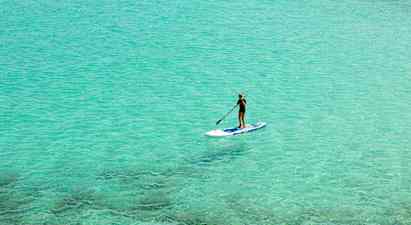 Person som paddlar stående på en paddleboard i klart turkost vatten. (AI-genererad text)