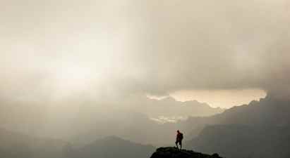 En vandringsman står på en bergstopp med dimmiga dalar och berg i bakgrunden. (AI-genererad text)