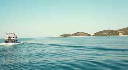 En båt färdas över ett stilla hav med några låga öar i horisonten. (AI-genererad text)