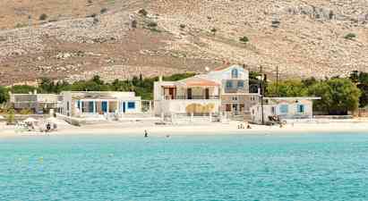 Bild av en klarblå havsvik med en sandstrand som har hus och kullar i bakgrunden. (AI-genererad text)