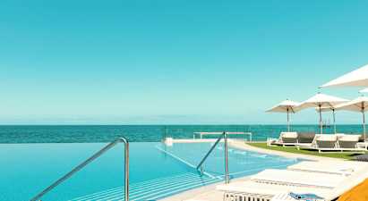 En infinitypool med utsikt över havet, omgiven av solstolar och parasoller. (AI-genererad text)