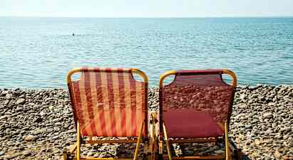 Två solstolar står på en stenig strand framför havet. (AI-genererad text)