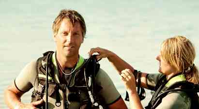 Två personer i dykarutrustning står i grunt vatten. (AI-genererad text)