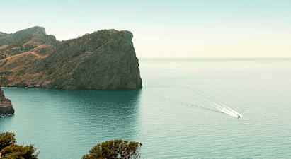 En klippa vid en kust med en båt som kör på vattnet. (AI-genererad text)