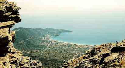 Utsikt från ett berg över kustlandskap med blått hav, gröna skogar och bebyggda områden. (AI-genererad text)