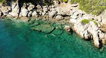 Klart turkost vatten vid en klippig kust, där personer snorklar nära ytan. (AI-genererad text)