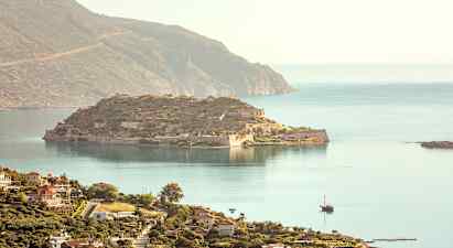 En vy över en historisk ö med ruiner och omgivande hav, och i förgrunden syns en kuststad med byggnader. (AI-genererad text)