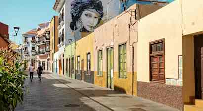 Färgglada husfasader längs en gångväg med två personer som promenerar. (AI-genererad text)