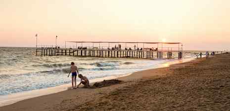 Strand med vågor vid solnedgång, träbrygga med personer ovanpå. (AI-genererad text)