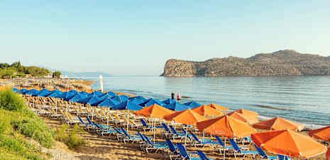 Strand med solstolar och parasoller, samt hav och klippor i bakgrunden. (AI-genererad text)